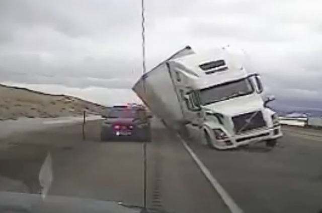 فيديو : الرياح تدفع مقطورة للانقلاب علي جانبها لتسحق سيارة شرطة !!